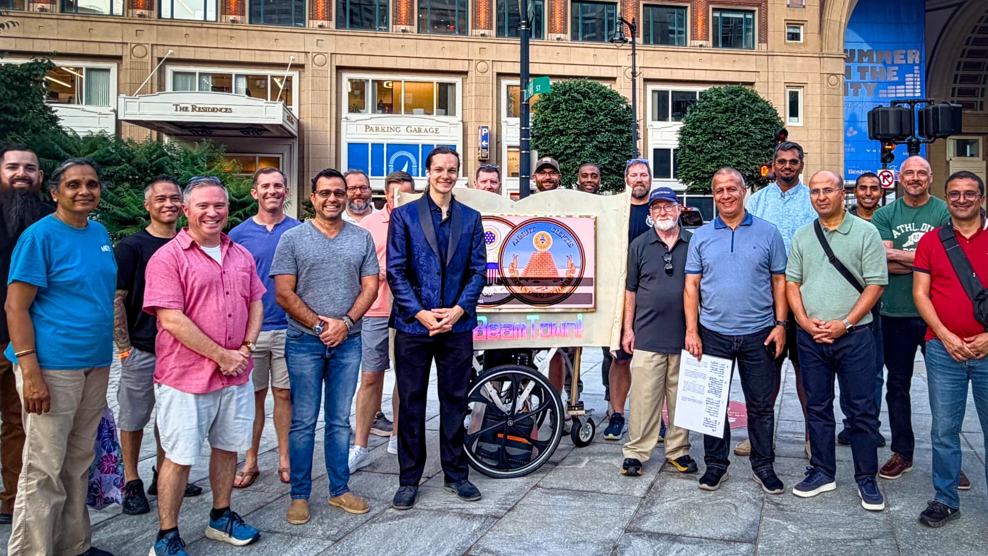 A United States Africa Command group of about twenty gathered around the Beamcaster on a Boston plaza at the end of their private walk, the lit scroll reading BeamTown